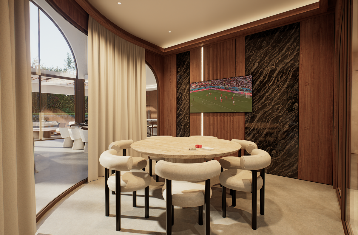 A modern dining room interior with a round light wood table surrounded by six upholstered chairs in cream and black. The room features warm wood paneling, dark marble wall accents, and a built-in television mounted on the wall showing a soccer match.