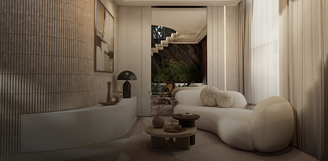 A modern living room interior featuring a curved cream-colored sofa with decorative pillows, a low round coffee table, a textured beige wall, and a large window looking out onto a staircase.